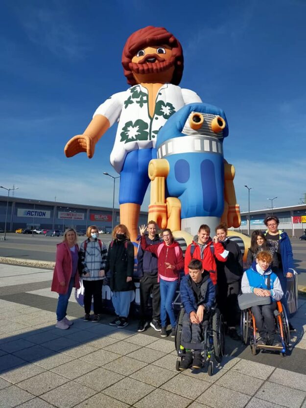 uczestnicy wycieczki stoją przy dmuchanym logo playmobil