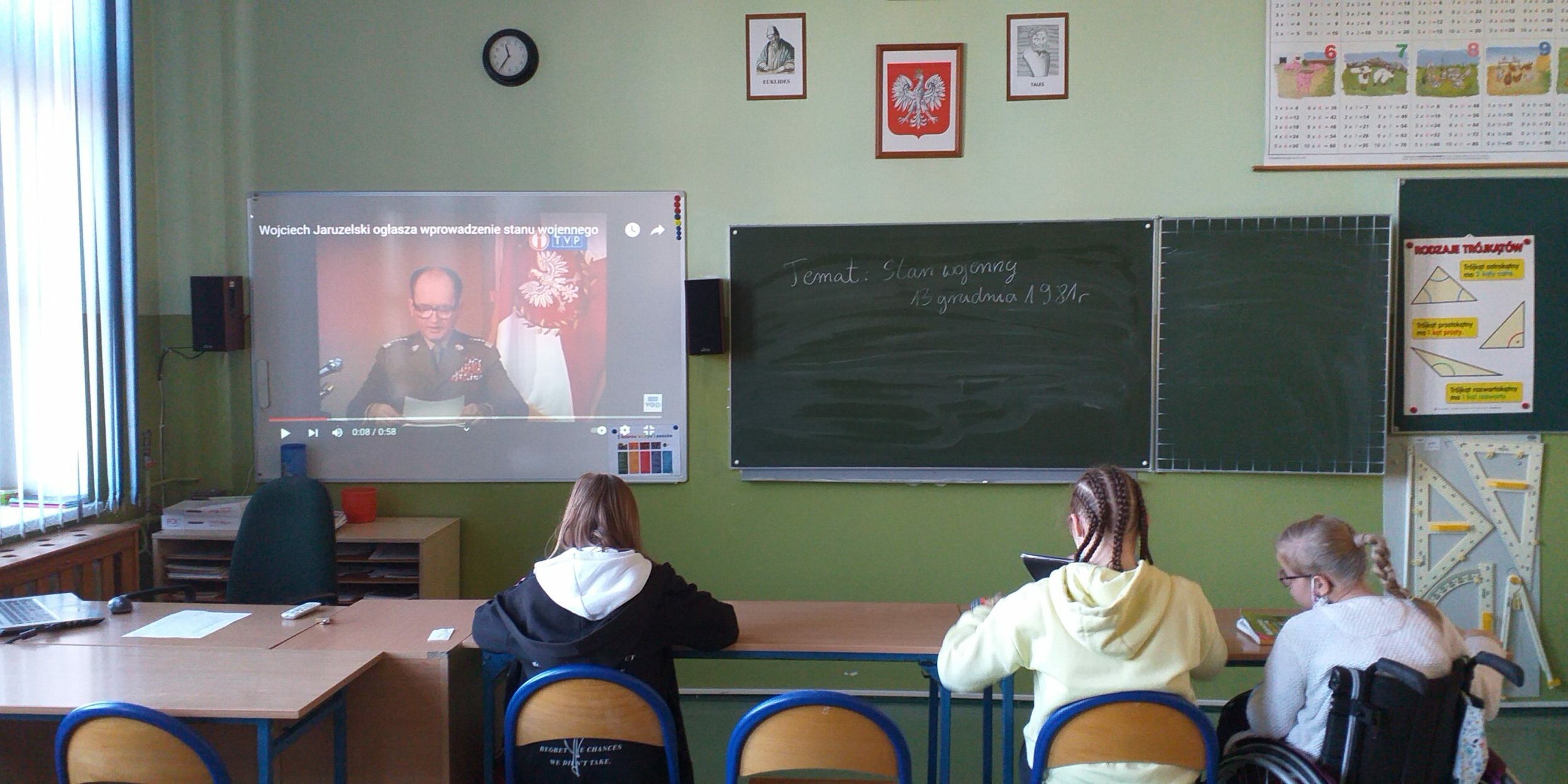 Uczniowie w klasie na dużym ekranie w klasie oglądają przemówienie generała Jaruzelskiego wprowadzające stan wojenny w Polsce.