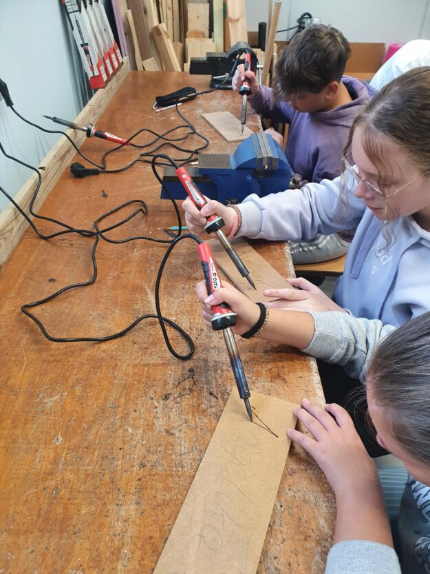 Uczniowie wykorzystują wypalarki do drewna podczas tworzenia wizytówek.