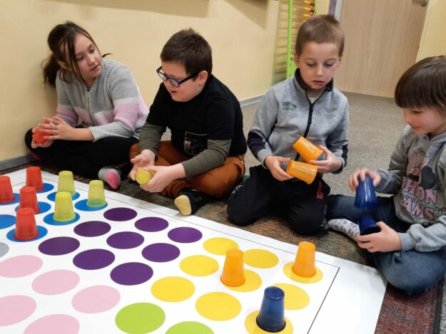Uczniowie układają kubki na macie edukacyjnej