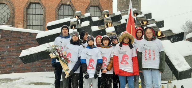 uczniowie szkoły wraz z nauczycielem stoją przed pomnikiem poległych górników.