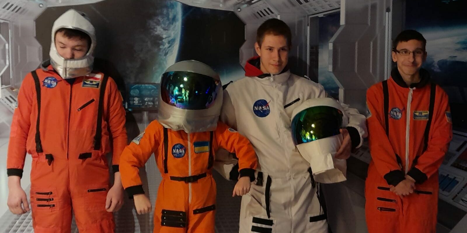 czterech uczniów stoi w strojach astronauty na tle wnętrza statku kosmicznego