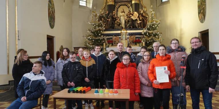 członkowie zespołu wraz z księdzem biskupem i przedstawicielem miasta na wspólnym zdjęciu na tle ołtarza w kościele w Zabrzu