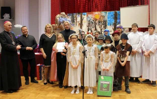 uczniowie występujący w jasełkach wraz z nauczycielami, dyrektorami oraz księdzem biskupem stoją razem do pamiątkowego zdjęcia