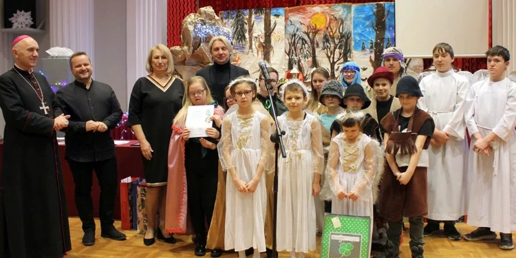 uczniowie występujący w jasełkach wraz z nauczycielami, dyrektorami oraz księdzem biskupem stoją razem do pamiątkowego zdjęcia