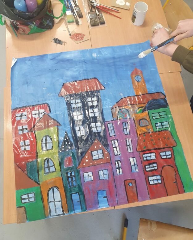 uczniowie malują plakat z budynkami mieszkalnymi.