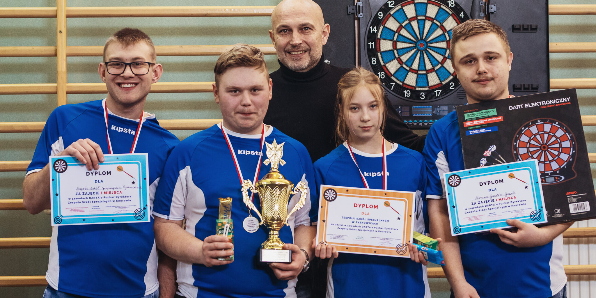 zwycięski zespół stoi z medalami, pucharem i dyplomami wraz z nauczycielem