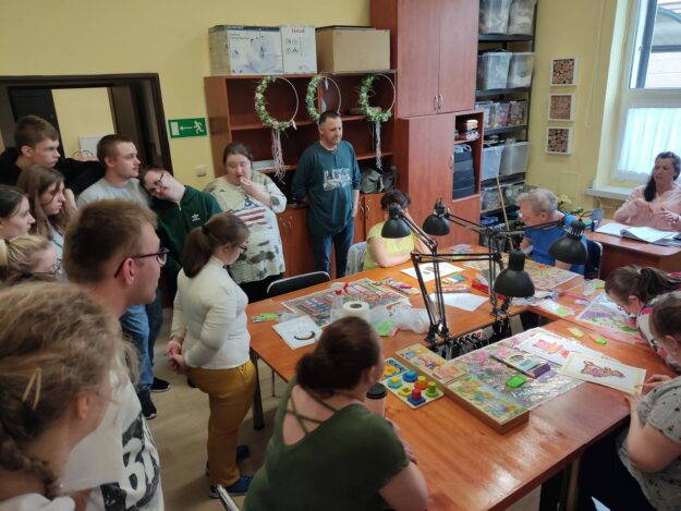 uczestnicy wycieczki obserwują pracę w pracowni zdobniczej, wyklejanie haftem diamentowym