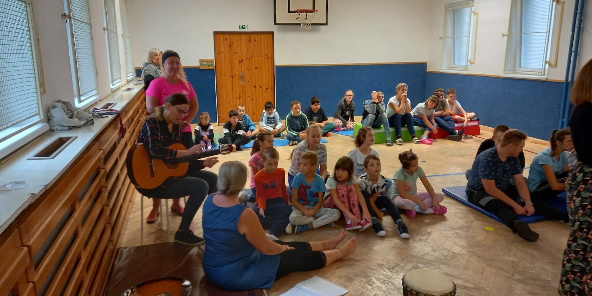 uczniowie siedzą na materacach i ćwiczą grę na instrumentach