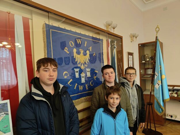 czterech uczniów stoi obok gabloty ze sztandarem Powiatu Gliwickiego