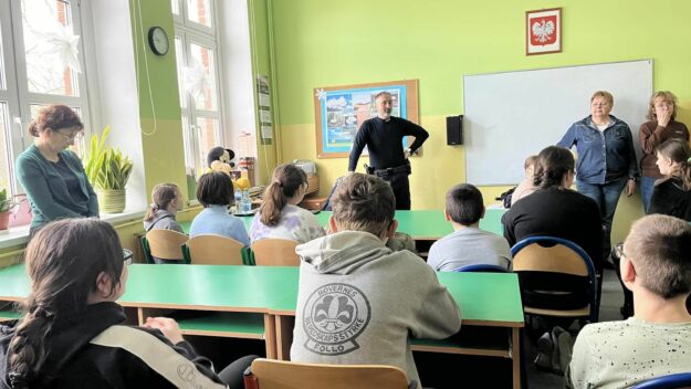 uczniowie zgromadzeni w sali słuchają prelekcji policjanta