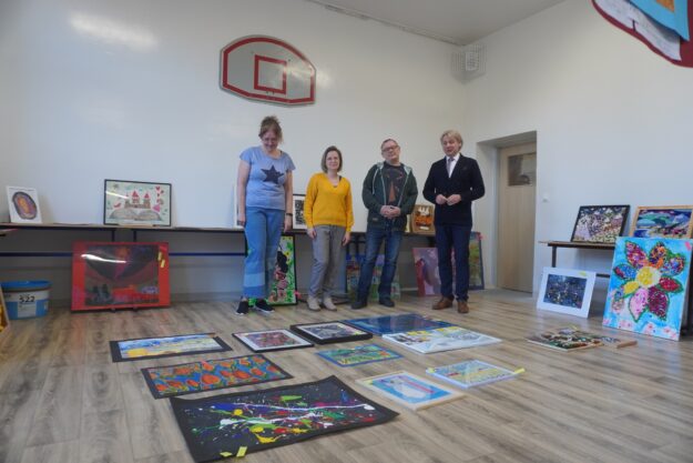 czworo jurorów stoi  w sali, w której wystawione są nadesłane prace plastyczne