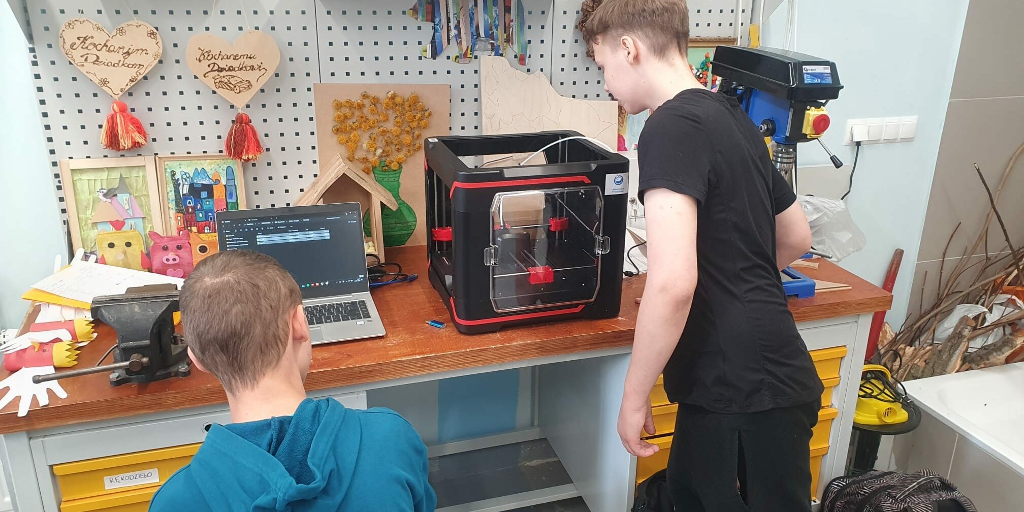 uczniowie obserwują pracującą drukarkę 3D