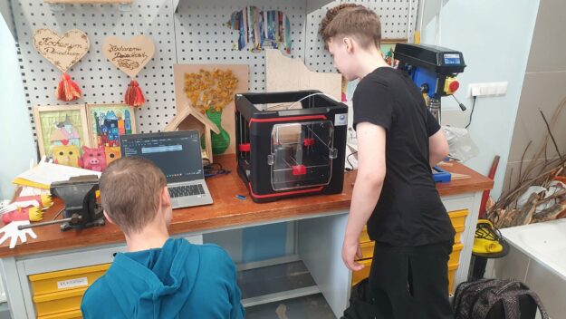 uczniowie obserwują pracującą drukarkę 3D