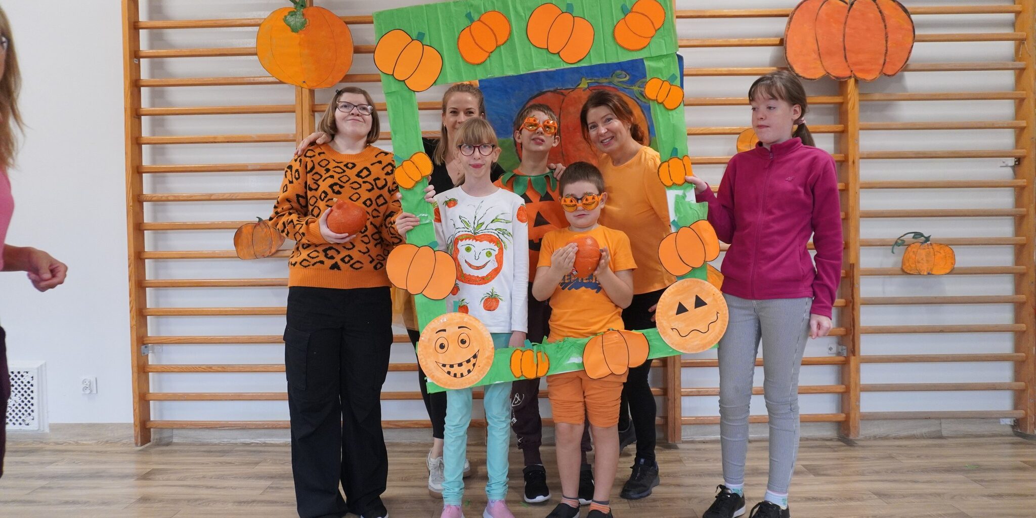 nauczyciel wraz z klasą stoją przy obramowaniu z dyniami