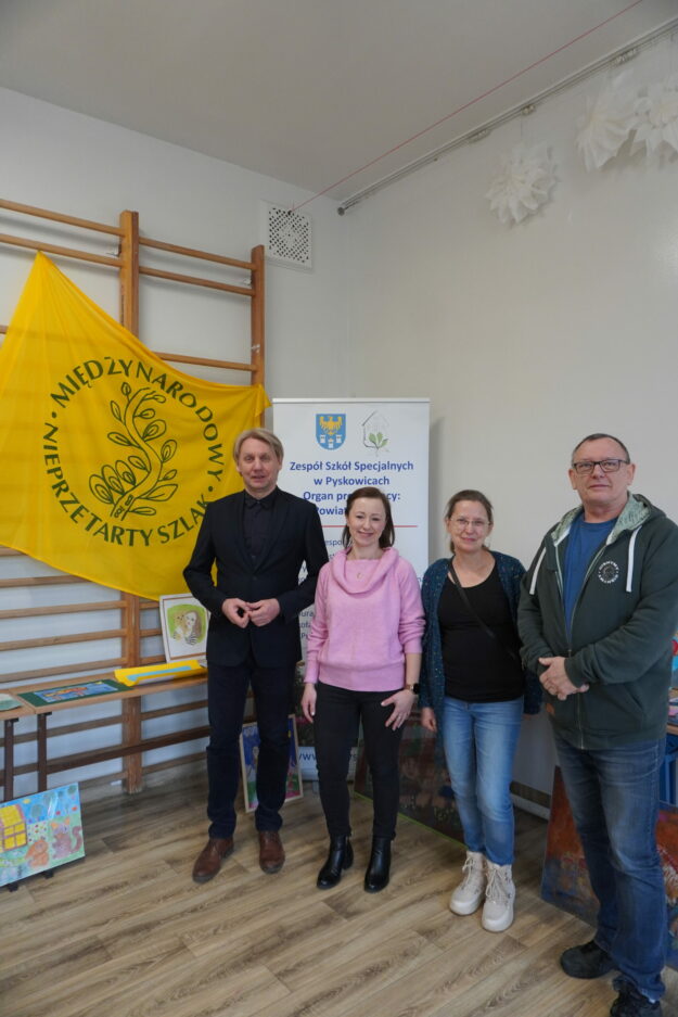 czworo jurorów stoi  w sali, w której wystawione są nadesłane prace plastyczne