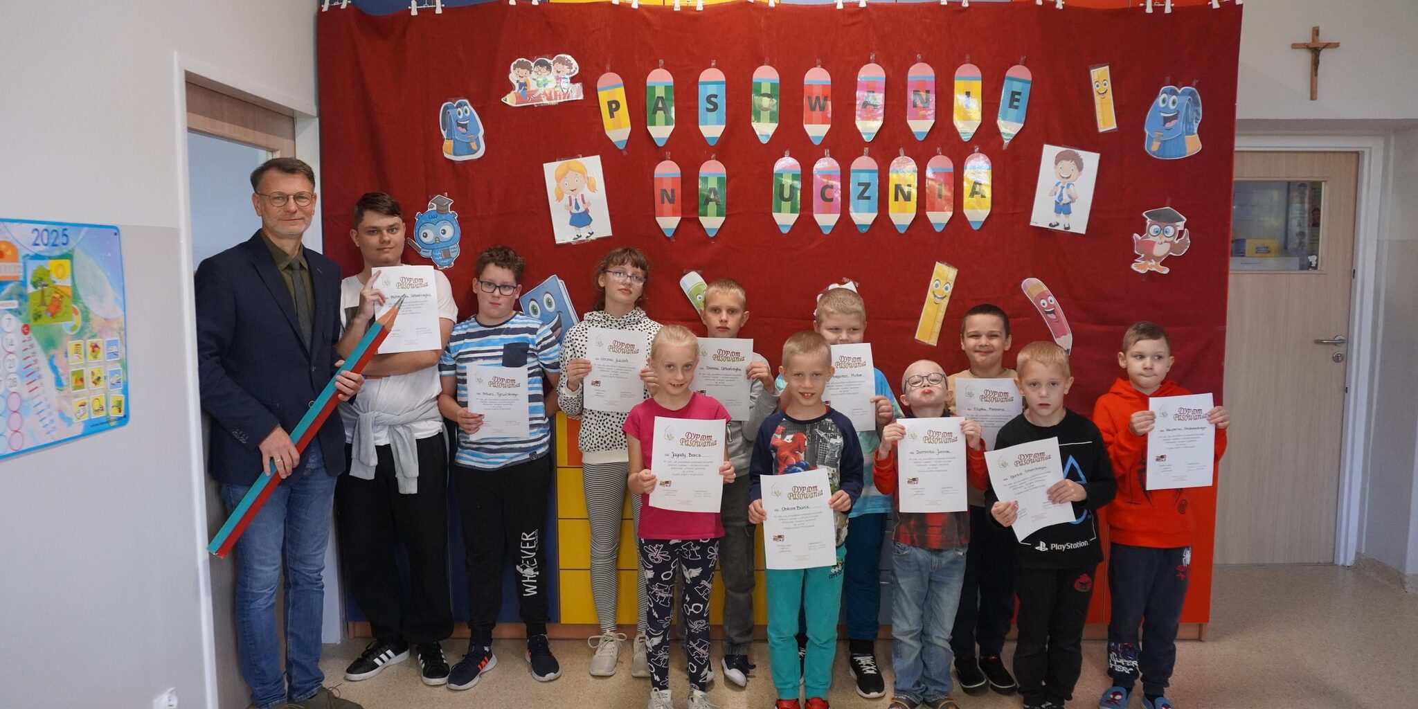 nowi uczniowie stoją w rzędzie z dyplomami pasowania na ucznia wraz z nauczycielkami i wicedyrektorem szkoły