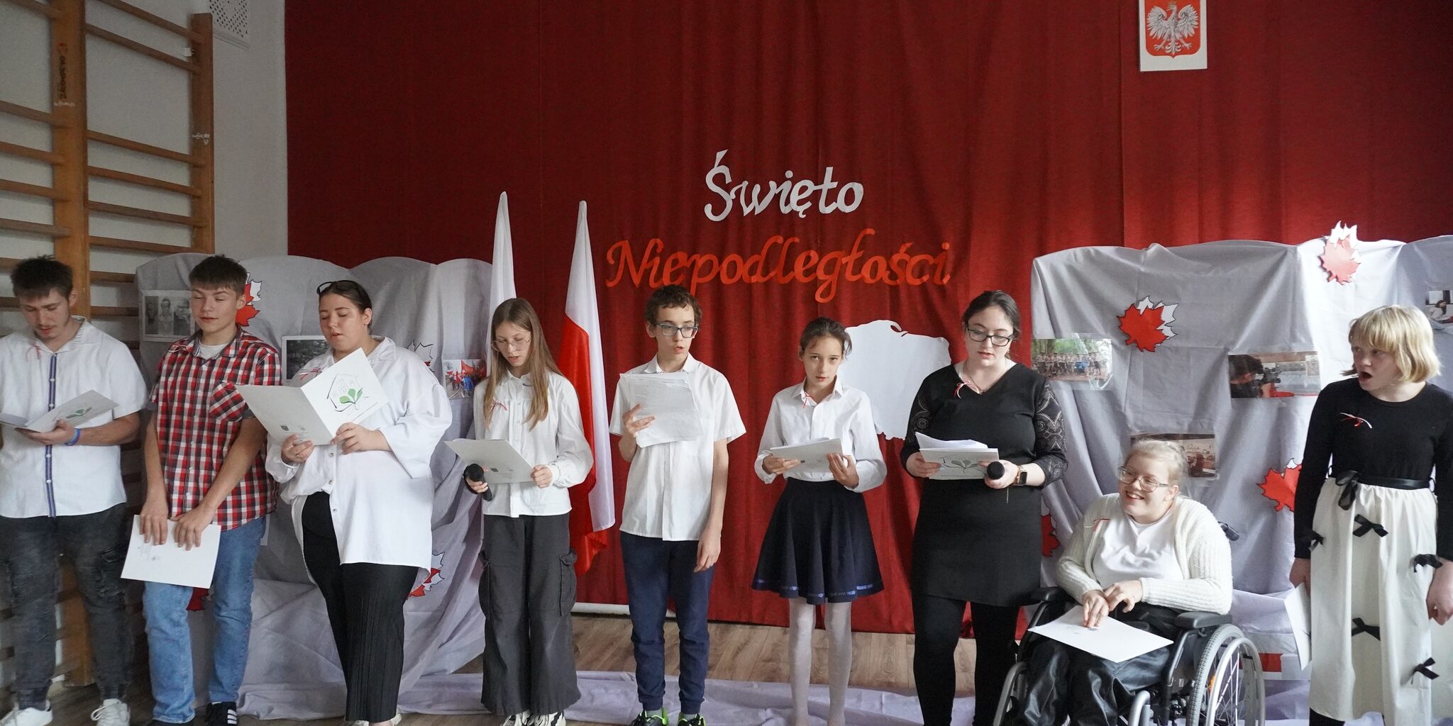 uczniowie występujący na tle dekoracji niepodległościowej