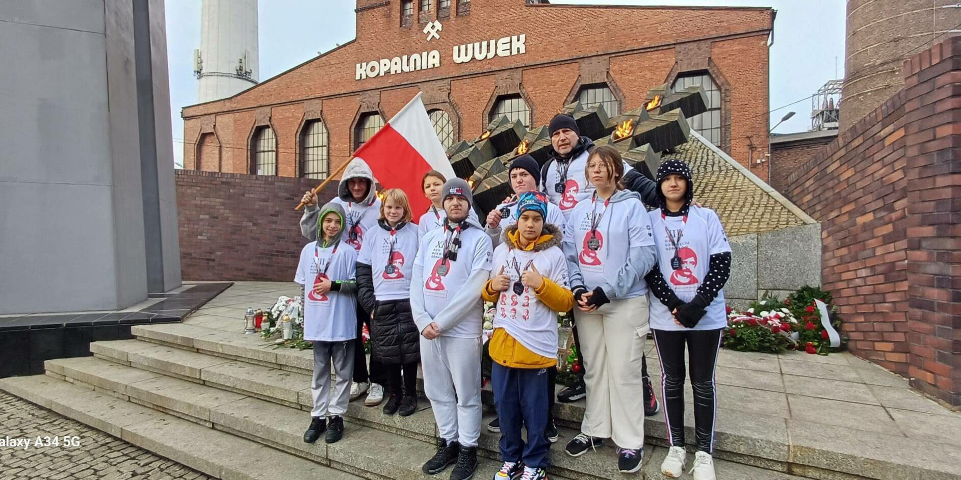 uczniowie wraz z nauczycielem stoją przed pomnikiem poległych górników